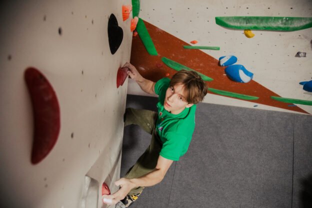 Bouldering boy on a climbing wall in green tshirt