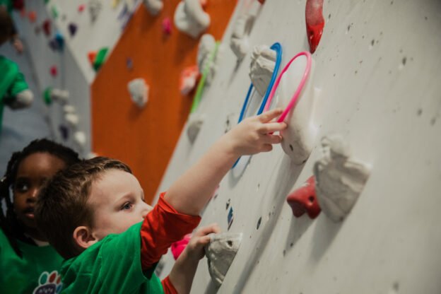 Small child in green tshirt adding a hoop to a climbing hold